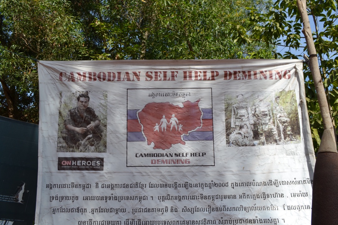 A banner for Cambodian Self Help Demining with a map of Cambodia, a photo of founder Aki Ra and a CNN Heroes logo